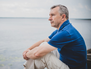 Gen X male sitting on a lake shore, thinking to himself