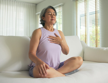 Millennial female sitting on a couch in a meditative position with eyes closed, taking a deep breath