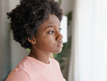 Gen Z female looking out the window with a melancholy expression